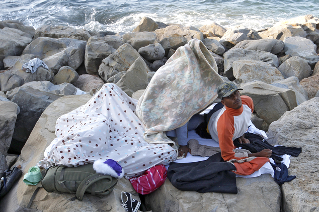 A migrant wakes up as he sleeps with others on the rocky beach at the France's Mediterranean border with Italy near Menton, southeastern France, Monday, June 15, 2015. French border police blocked border crossings last week, citing the influx of migrants, and about 200 would-be refugees have refused to leave the rocks of Ventimiglia, Italy, just a few kilometers from the swank resorts of Nice and Saint-Jean-Cap-Ferrat on the French Riviera. (AP Photo/Lionel Cironneau)
